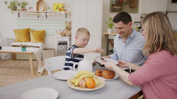 A happy family with down syndrome son at the table, having breakfast.