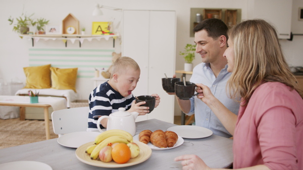 A happy family with down syndrome son at the table, having breakfast.