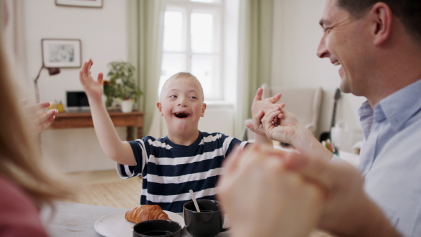 A happy family with down syndrome son at the table, having breakfast and fun.