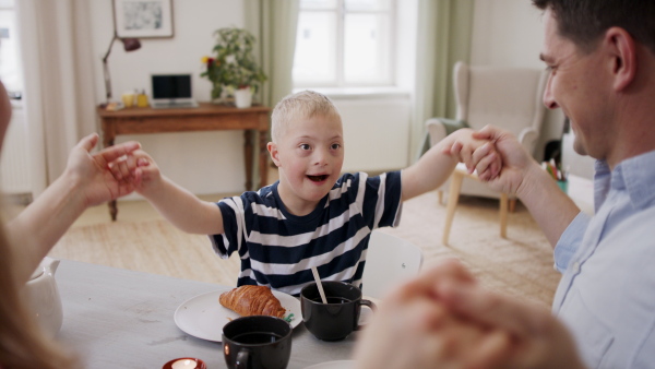 A happy family with down syndrome son at the table, having breakfast and fun.