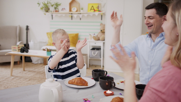 A happy family with down syndrome son at the table, having breakfast and fun.