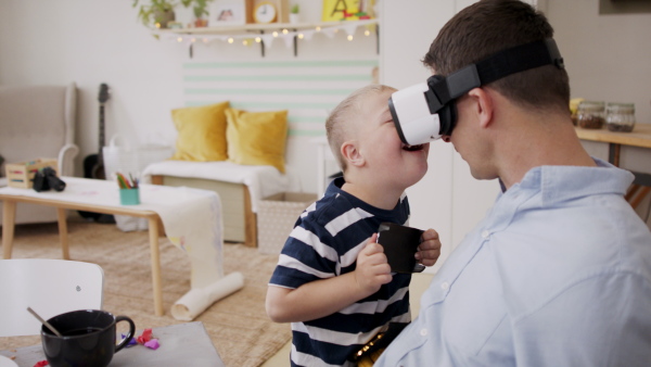 A father with happy down syndrome son indoors at home, using vr goggles.