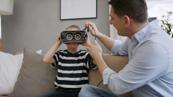 A father with happy down syndrome son indoors at home, using vr goggles.