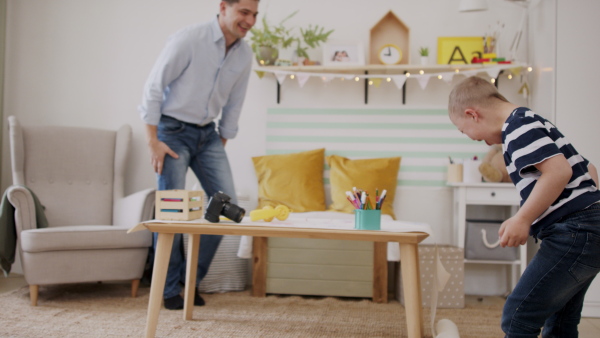 Father with happy down syndrome son indoors at home, having fun laughing.