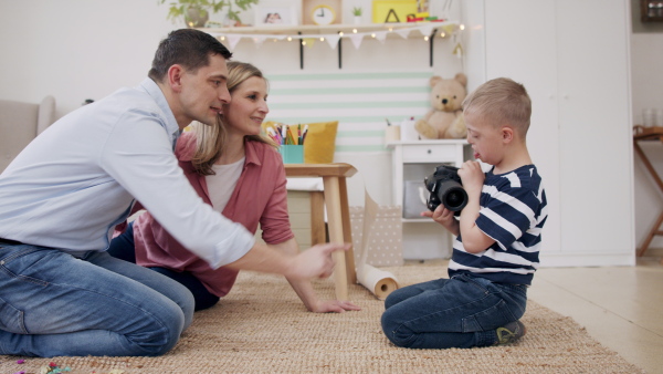 A family with happy down syndrome son indoors at home, using camera and taking pictures.