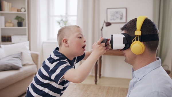 A father with happy down syndrome son indoors at home, using vr goggles.