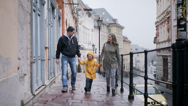 Portrait of happy family with down syndrome son outdoors on a walk in rain, having fun.