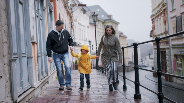 A happy family with down syndrome son outdoors on a walk in rain, having fun.