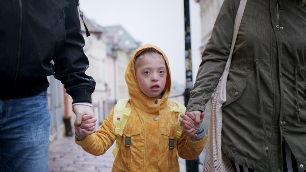 A happy family with down syndrome son outdoors on a walk in rain.