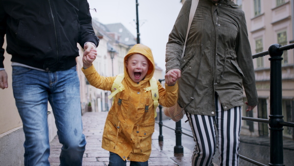 Portrait of happy family with down syndrome son outdoors on a walk in rain, having fun.