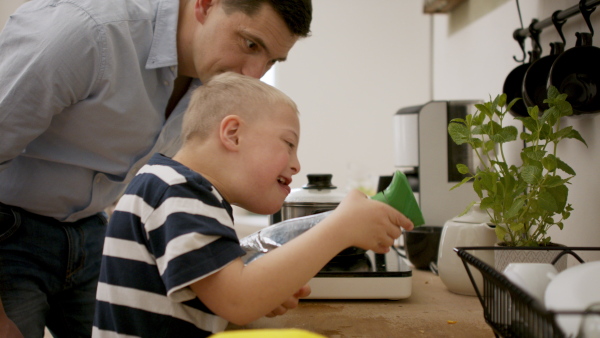 A father with happy down syndrome son indoors in kitchen, cleaning kitchen counter.