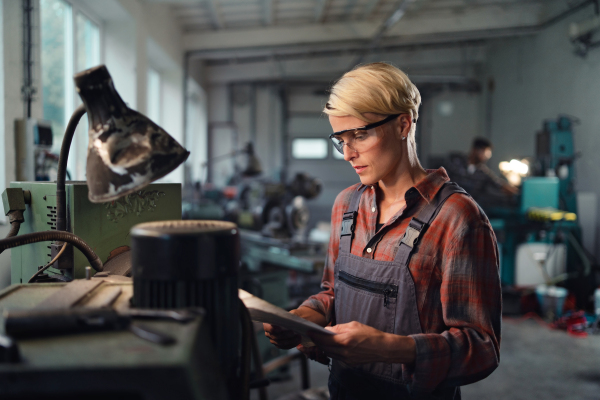 A portrait of young industrial woman working indoors in metal workshop.