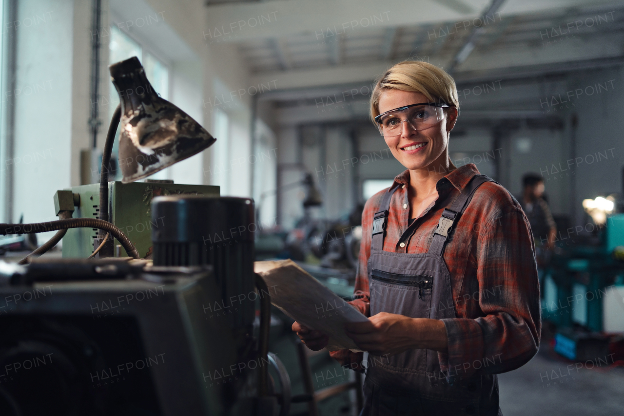 A portrait of mid adult industrial woman working indoors in metal workshop, looking at camera.