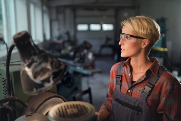 A portrait of young industrial woman working indoors in metal workshop.