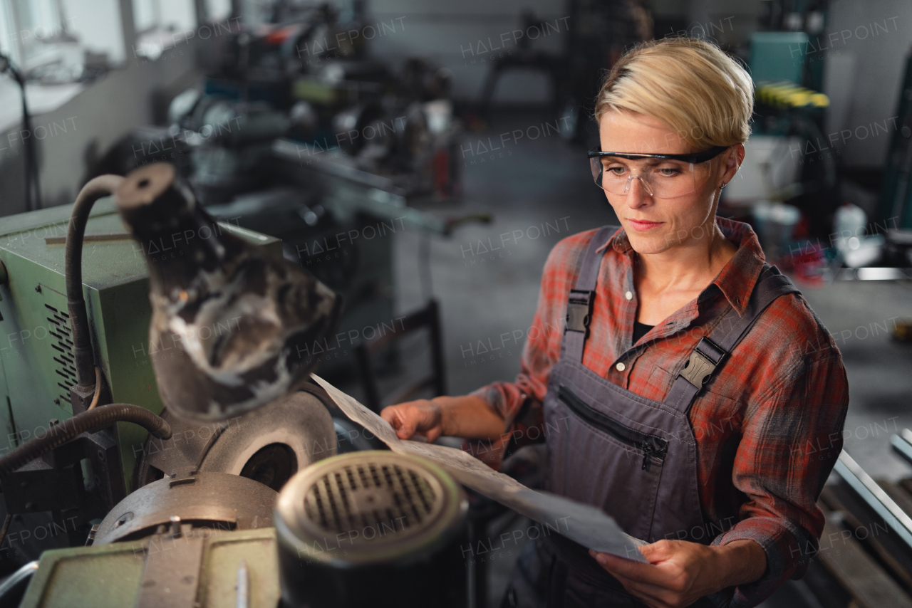 A portrait of young industrial woman working indoors in metal workshop.