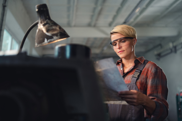 A portrait of young industrial woman working indoors in metal workshop.