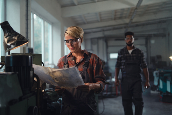 A portrait of young biracial industrial colleagues working indoors in metal workshop, smiling