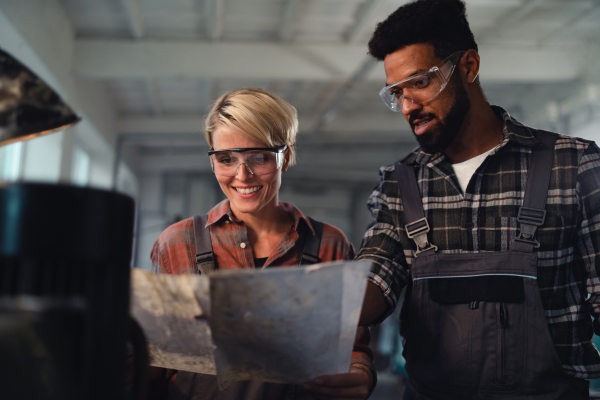 A portrait of young biracial industrial colleagues working indoors in metal workshop, smiling