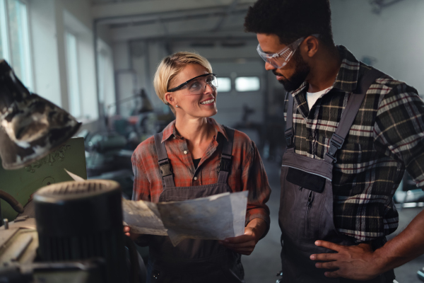 A portrait of young biracial industrial colleagues working indoors in metal workshop, smiling