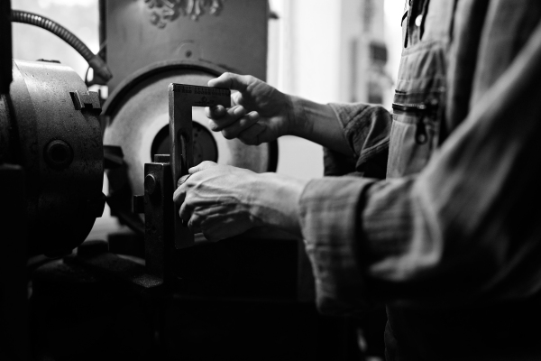 Black and white close up of a man hand with caliper measure steel component indoors in metal workshop.