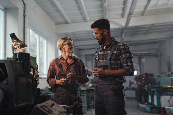 A portrait of young biracial industrial colleagues working indoors in metal workshop.