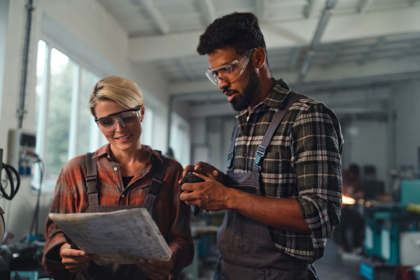 A portrait of young biracial industrial colleagues working indoors in metal workshop, smiling