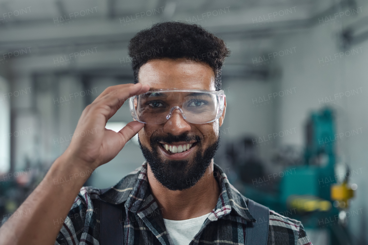 A portrait of happy young industrial man working indoors in metal workshop, looking at camera.