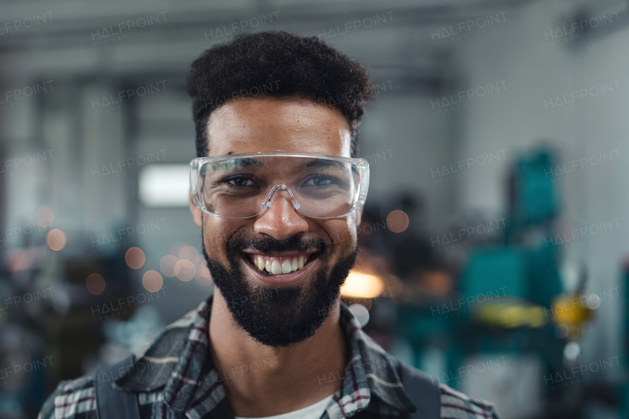 A portrait of happy young industrial man working indoors in metal workshop, looking at camera.