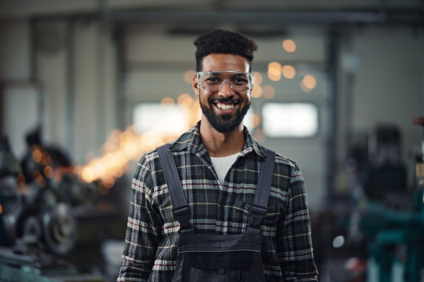 A portrait of young industrial man working indoors in metal workshop, looking at camera.