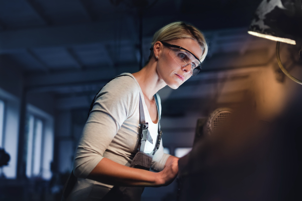 A portrait of young industrial woman working indoors in metal workshop.