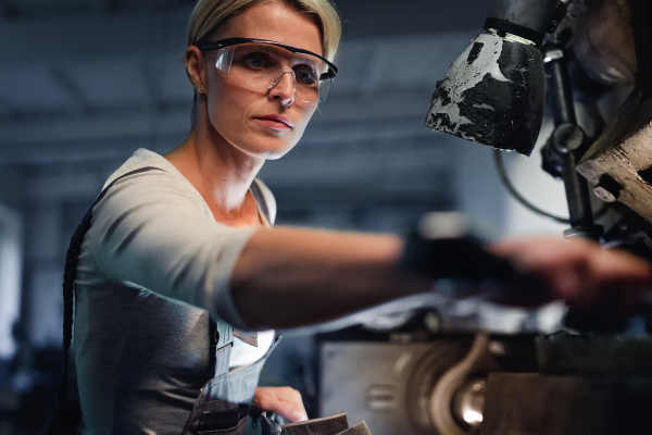 A portrait of mid adult industrial woman working indoors in metal workshop.