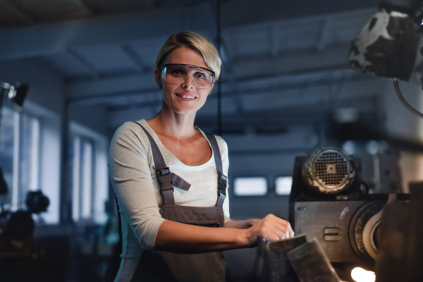 A portrait of mid adult industrial woman working indoors in metal workshop, looking at camera.