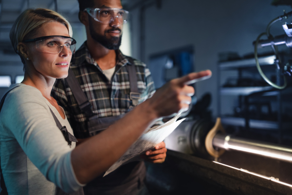 A portrait of young biracial industrial colleagues working indoors in metal workshop.