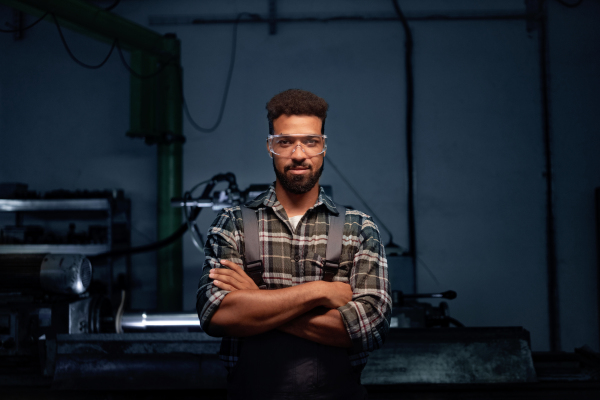 A portrait of young industrial man working indoors in metal workshop, looking at camera.