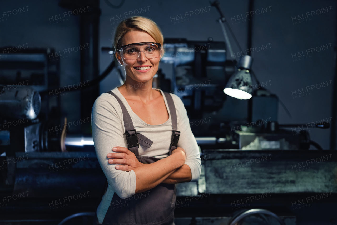 A portrait of mid adult industrial woman working indoors in metal workshop, looking at camera.