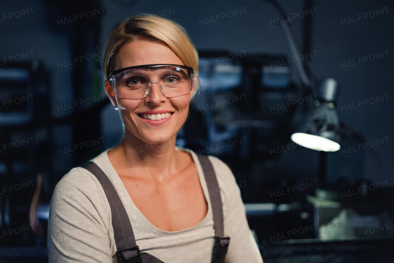 A portrait of mid adult industrial woman working indoors in metal workshop, looking at camera.