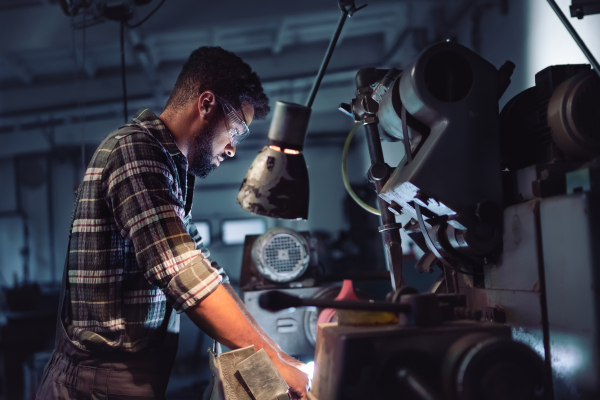 Portrait of a young concentrated african american industrial man working on cutter indoors in metal workshop.