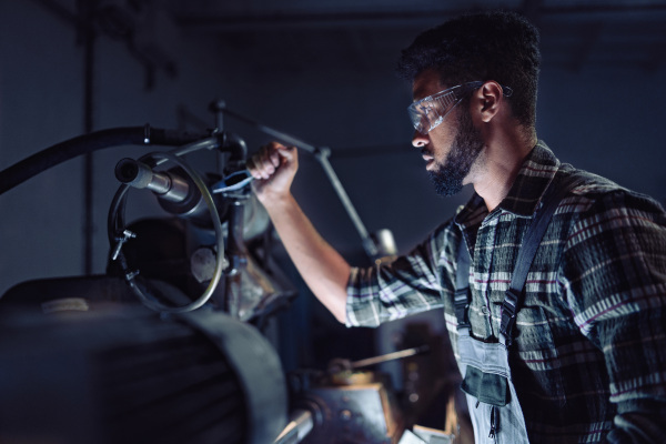 Portrait of a young concentrated african american industrial man working on cutter indoors in metal workshop.