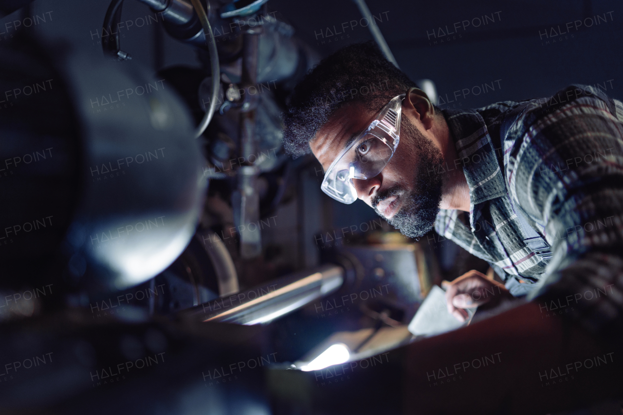 A close up of young concentrated african american industrial man working on cutter indoors in metal workshop.