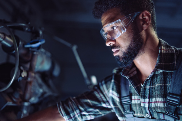 A close up of young concentrated african american industrial man working on cutter indoors in metal workshop.