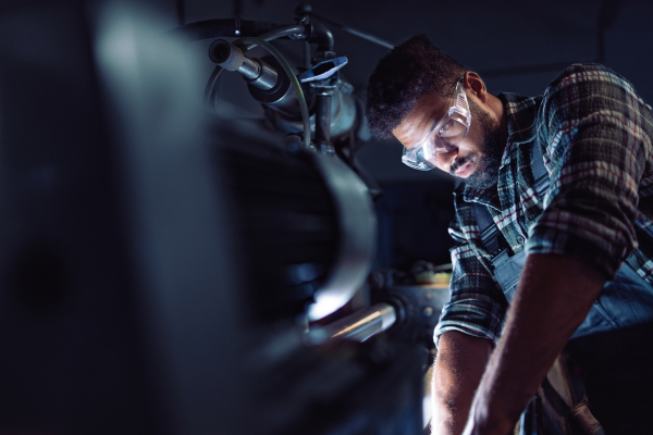 A close up of young concentrated african american industrial man working on cutter indoors in metal workshop.