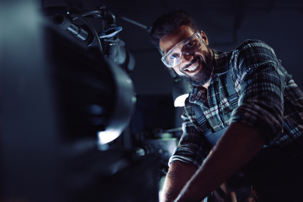 A close up of young concentrated african american industrial man working on cutter indoors in metal workshop.