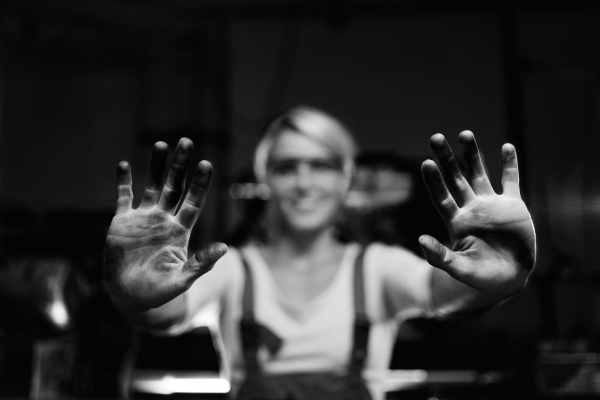 A young woman worker showing her dirty hands indoors in metal workshop