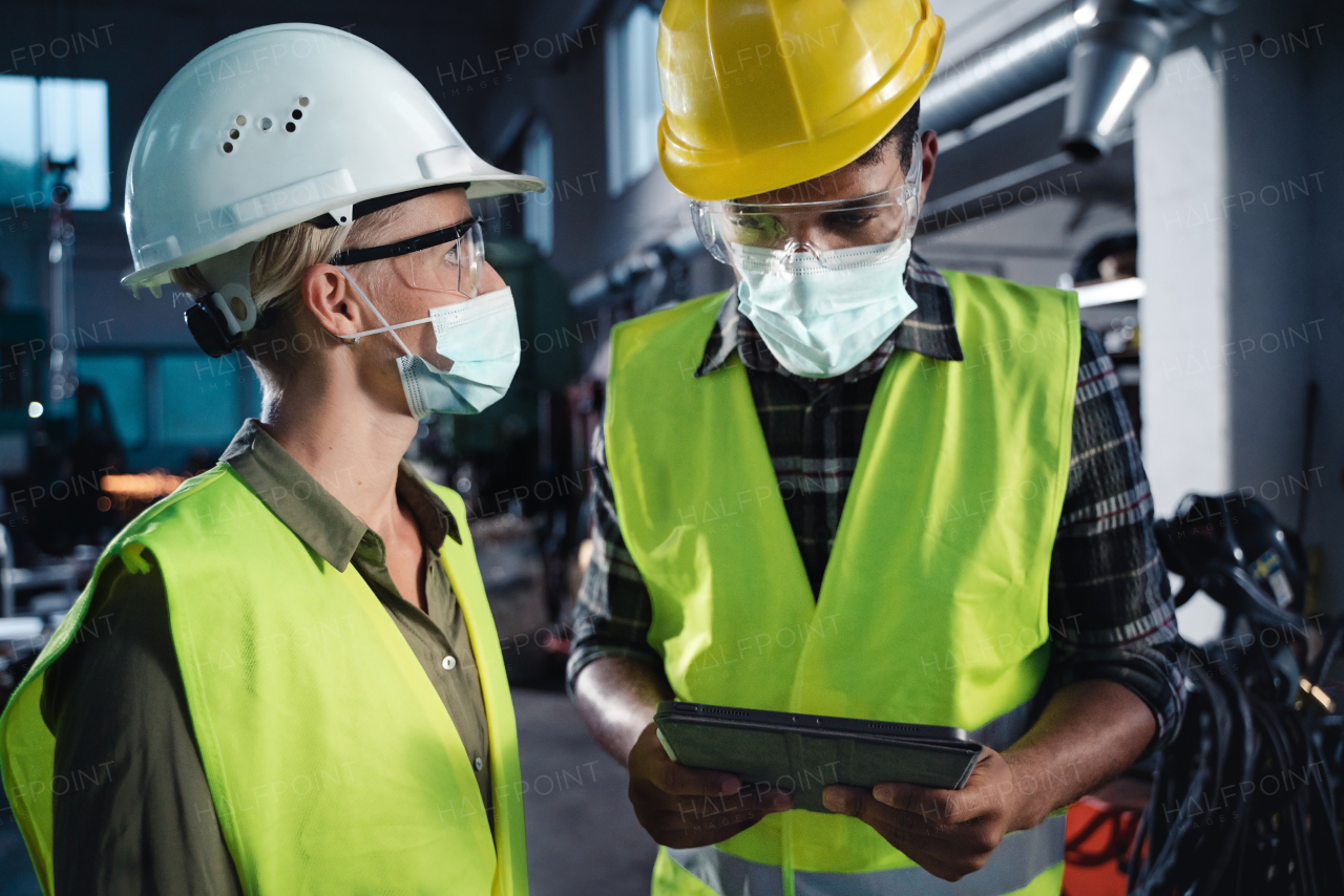 A portrait of industrial inspectors with face masks doing a general check up indoors at metal workshop, coronavirus concept.