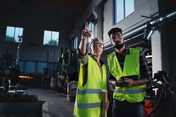 A portrait of industrial inspectors doing a general check up indoors at metal workshop.