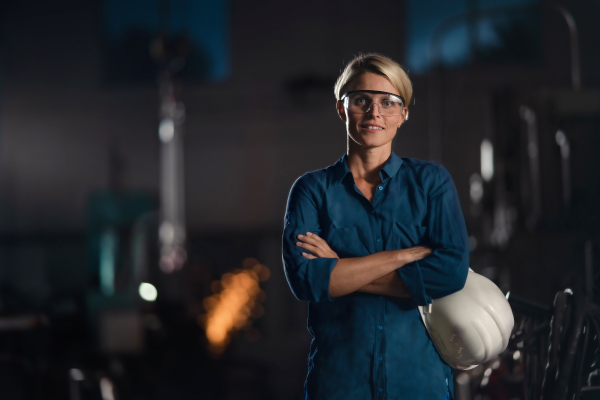 A portrait of mid adult industrial woman working indoors in metal workshop, looking at camera.