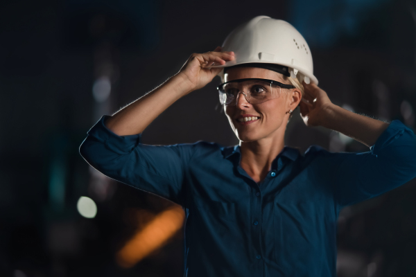 A portrait of mid adult industrial woman working indoors in metal workshop during night shift.