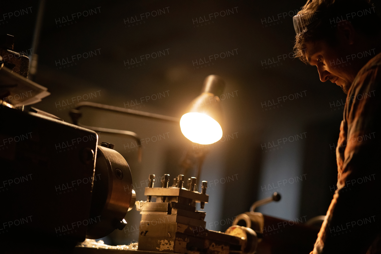 An industrial man working indoors in metal workshop at night.