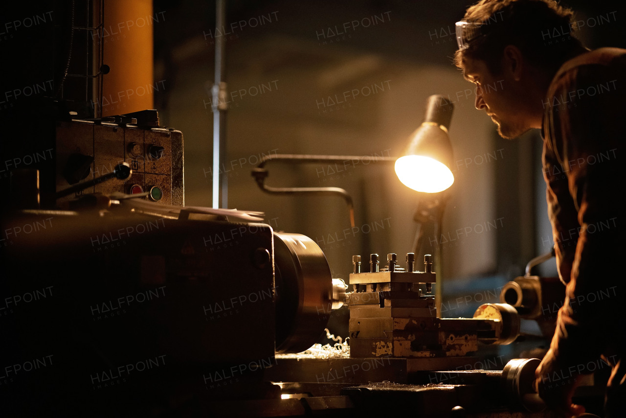 An industrial man working indoors in metal workshop at night.