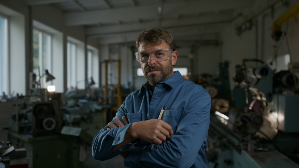 A mature industrial man working indoors in metal workshop, looking at camera.